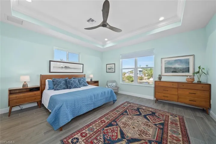 Bedroom with a tray ceiling, multiple windows, ceiling fan, and hardwood / wood-style flooring