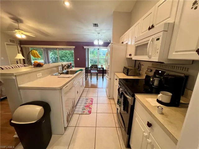Kitchen with light tile patterned flooring, a kitchen island with sink, and white cabinets