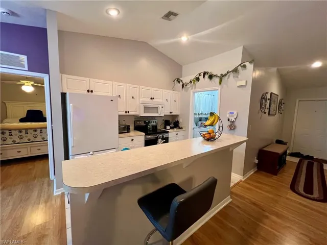 Kitchen with vaulted ceiling, white cabinetry, a kitchen breakfast bar.