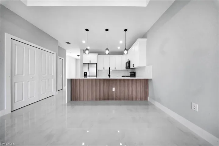 Kitchen featuring a peninsula, white cabinetry, stainless steel refrigerator with ice dispenser, pendant lighting, and black range