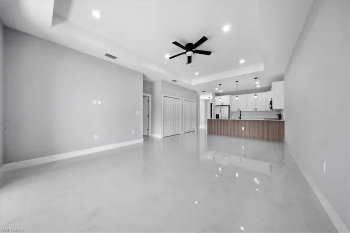 Unfurnished living room featuring a raised ceiling, ceiling fan, and recessed lighting