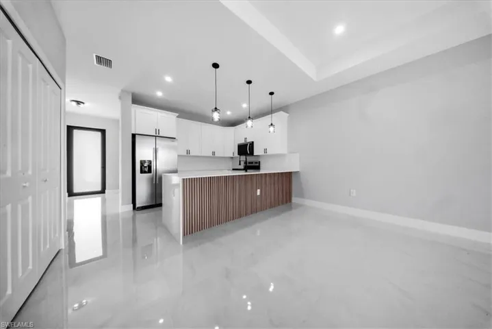 Kitchen with stainless steel appliances, a peninsula, white cabinets, decorative light fixtures, and recessed lighting