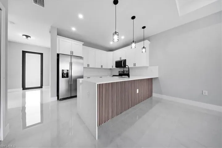 Kitchen featuring stainless steel appliances, white cabinets, hanging light fixtures, a peninsula, and light stone counters
