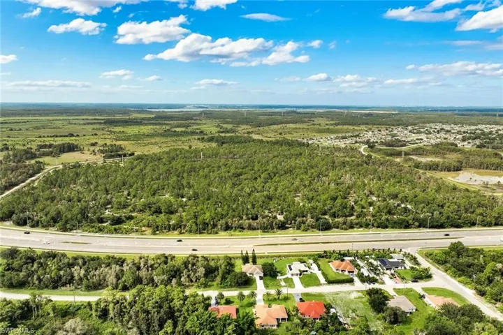 Expansive undeveloped land bordering a multi-lane highway, surrounded by substantial natural landscaping and residential developments
