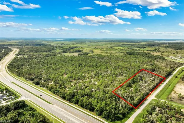 Expansive undeveloped land with a perimeter outline, adjacent to a paved road and a multi-lane highway