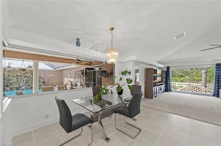 Open concept living area featuring a formal dining space with a contemporary chandelier, tile flooring, and a large window overlooking a stone-accented pool area