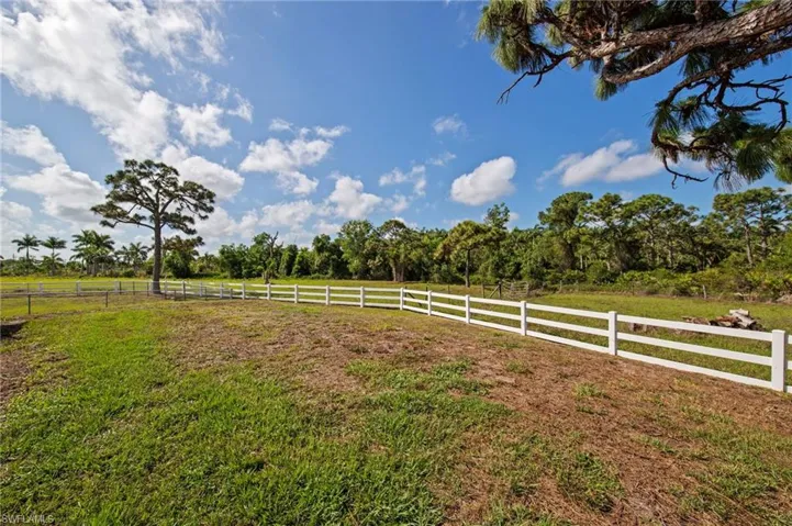 Expansive property featuring a white three-rail fence, a mature central tree, and surrounding natural foliage