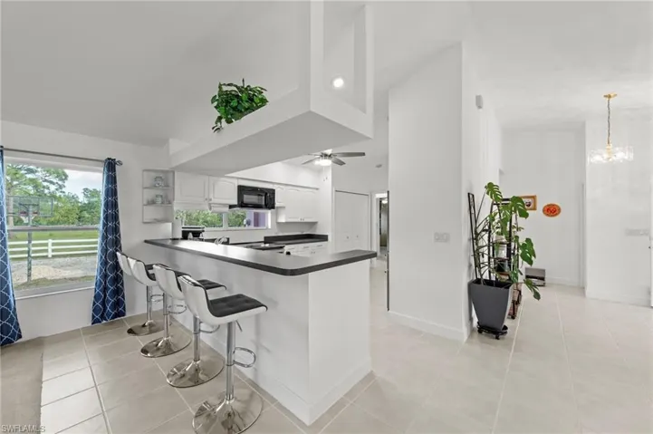 Kitchen featuring white cabinetry, dark countertops, built-in microwave, tile flooring, and a breakfast bar with seating