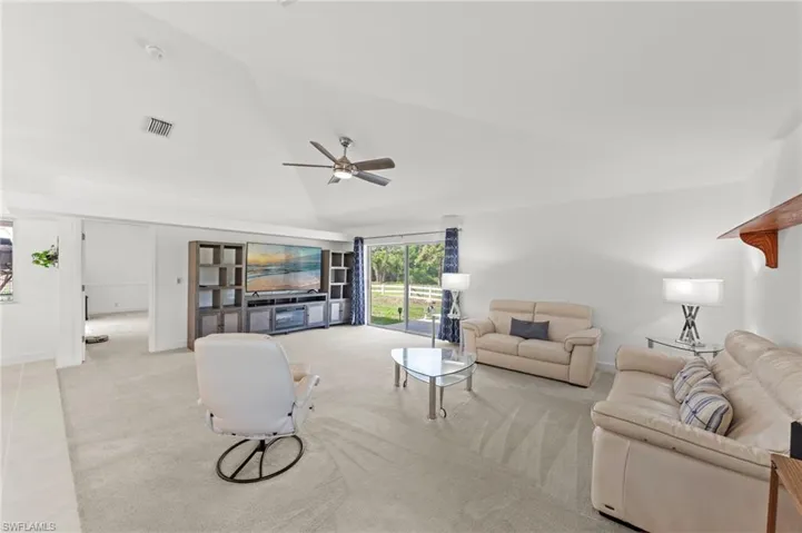 Spacious living area featuring a vaulted ceiling and light-toned carpet