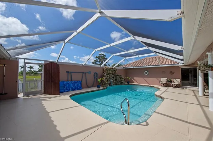 Screen-enclosed outdoor pool area featuring a freeform swimming pool with a waterfall rock feature, beige concrete decking, and a sliding glass door entry to the interior