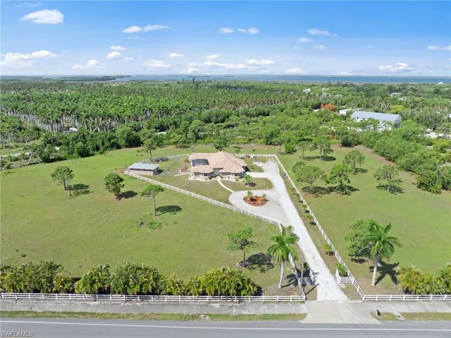 Expansive property featuring a circular driveway, white perimeter fencing, and mature palm trees