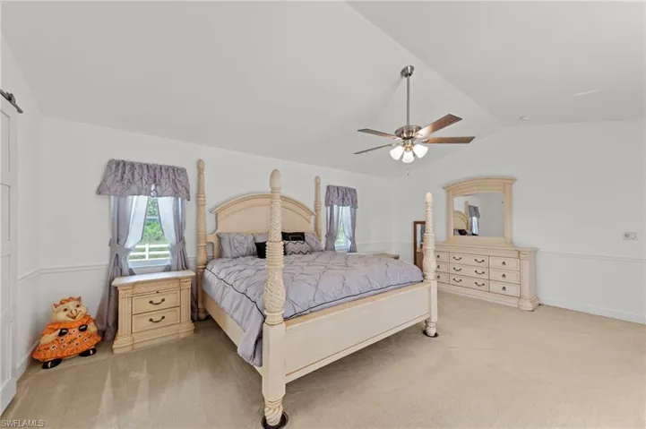 Spacious room featuring vaulted ceilings, a ceiling fan with integrated lighting, two windows, wainscoting, and carpet flooring