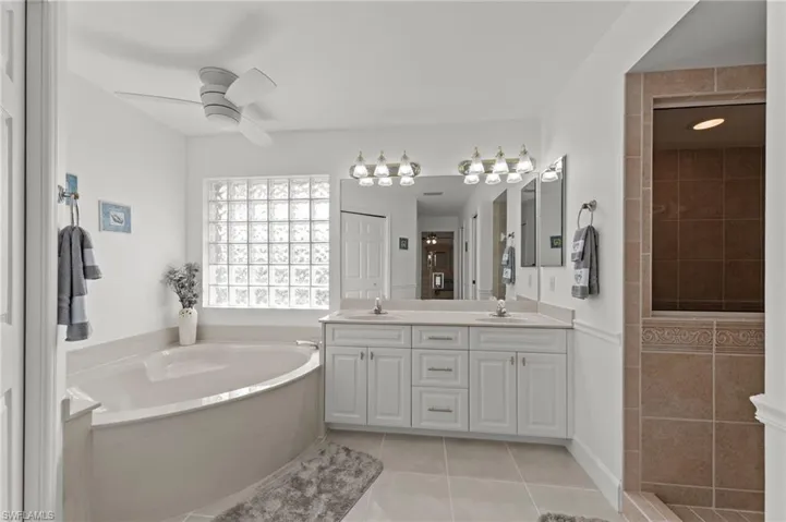 Bathroom featuring a corner soaking tub, glass block window, dual vanity with shaker-style cabinetry, and a walk-in shower with tiled walls