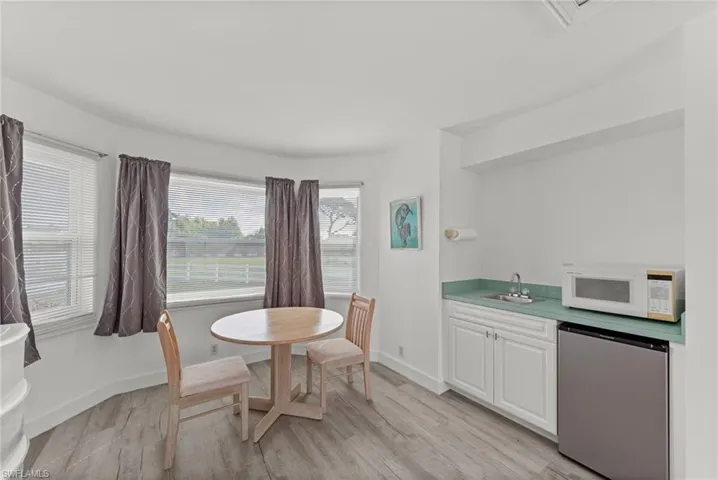 Room with wood-finish flooring, a bay window with multiple panes, and a built-in wet bar featuring white cabinetry and a light green countertop