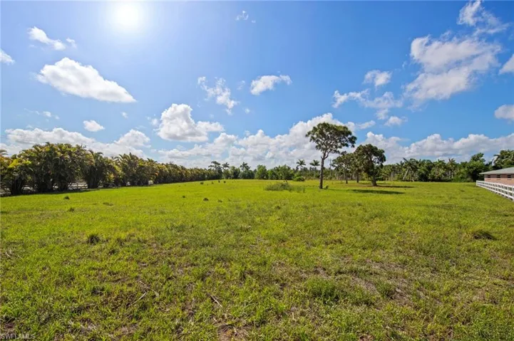 Expansive green field featuring mature trees and a partial white picket fence