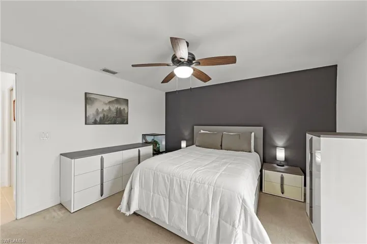 Carpeted bedroom featuring a dark accent wall, a ceiling fan with integrated lighting, and a white interior door