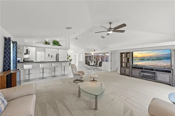 Spacious living area featuring vaulted ceilings, ceiling fan, and carpet flooring