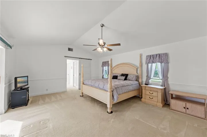 Vaulted ceiling bedroom with a ceiling fan, light beige carpet flooring, and white paneled walls
