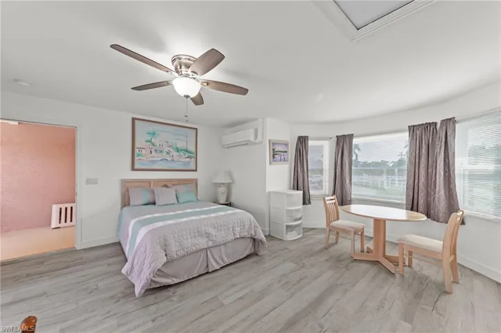 Spacious interior room featuring wood-finish flooring, a ceiling fan with integrated lighting, multiple windows with blinds and curtains, and a mini-split air conditioning unit