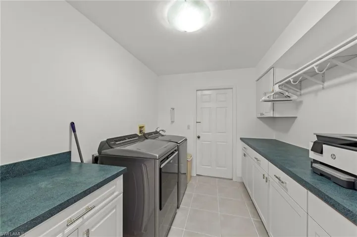 Dedicated utility room featuring light tile flooring, extensive countertop space, white cabinetry with silver hardware, and a clothes hanging rack
