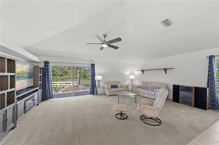 Spacious living area featuring expansive sliding glass doors, built-in shelving and media console, vaulted ceiling, neutral carpeting, and a ceiling fan