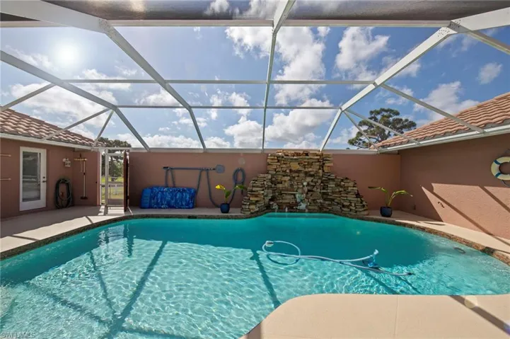 Screened-in pool area featuring a freeform swimming pool with a stone-clad waterfall, a surrounding concrete patio, and a light-colored tile roofline