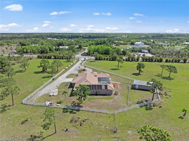 Expansive property with a tan-colored house featuring a screened-in pool enclosure, a long gravel driveway, a separate outbuilding, and a perimeter fence