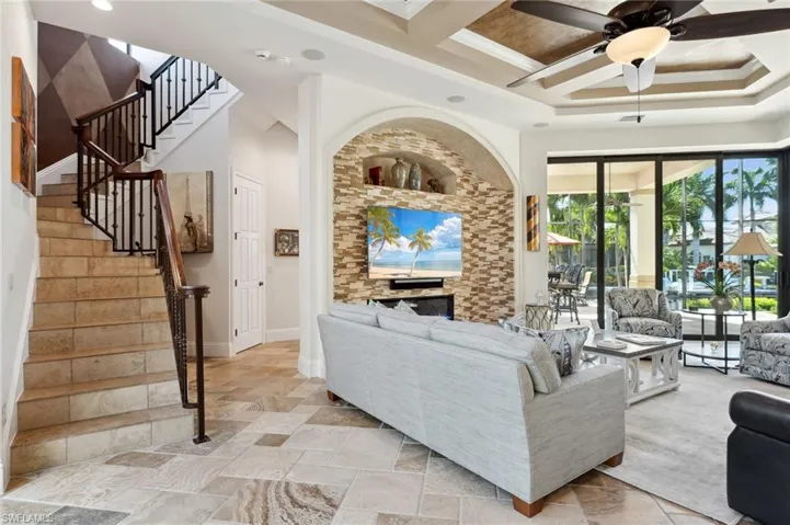 Living room with beamed ceiling, coffered ceiling, a fireplace, ornamental molding, and ceiling fan