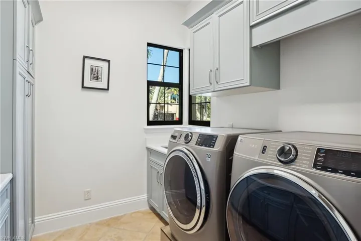 Clothes washing area featuring cabinets, light tile patterned floors, and washing machine and clothes dryer