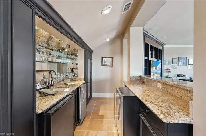 Bar with crown molding, vaulted ceiling, sink, and light stone counters