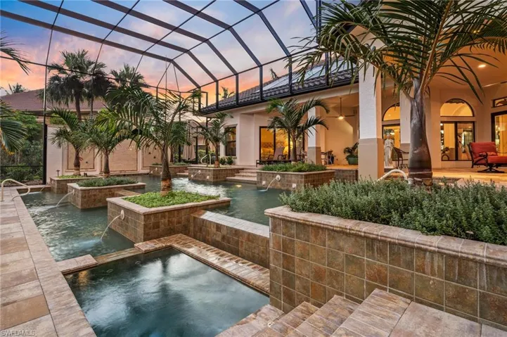Pool at dusk featuring a lanai, an in ground hot tub, a patio area, and pool water feature