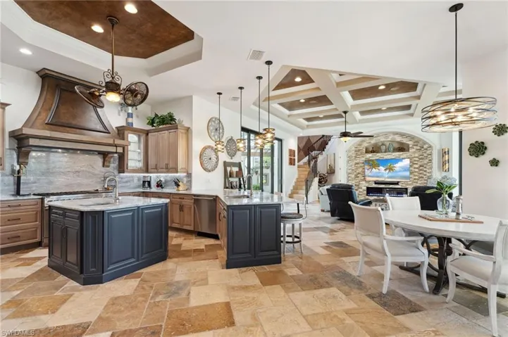 Kitchen featuring hanging light fixtures, a center island with sink, dishwasher, and light stone countertops