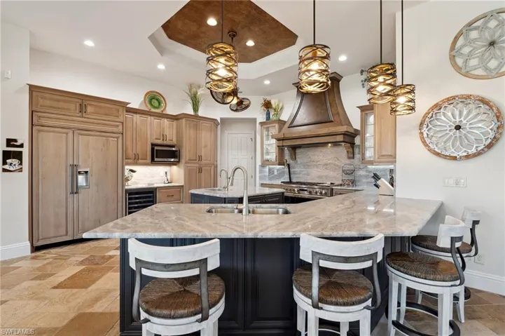 Kitchen with decorative light fixtures, paneled fridge, a tray ceiling, a kitchen breakfast bar, and decorative backsplash