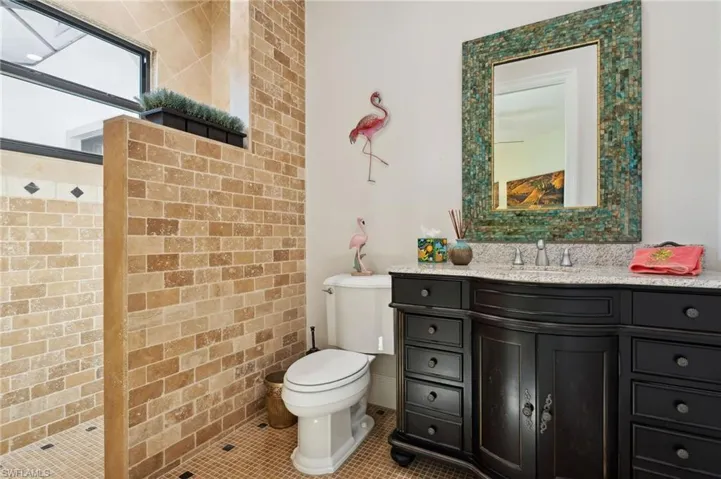 Bathroom with tile patterned flooring, a shower, brick wall, vanity, and toilet
