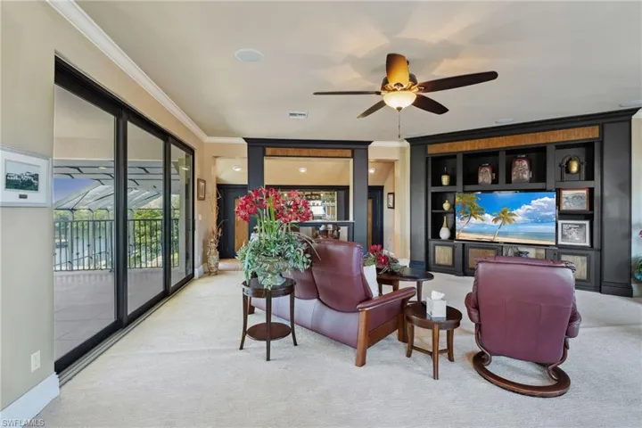 Living room with light carpet, ceiling fan, ornamental molding, and built in features