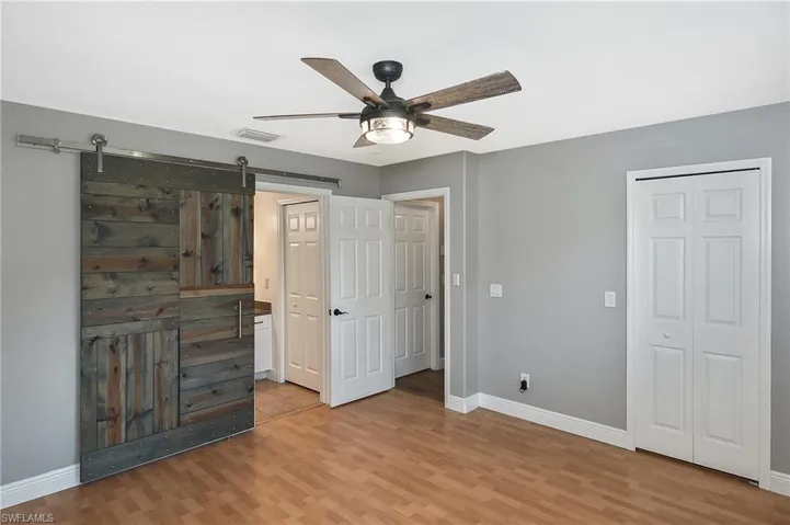 Unfurnished bedroom with ceiling fan, light wood-type flooring, and a barn door