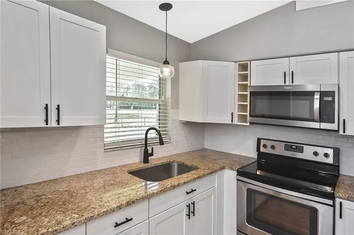 Kitchen featuring sink, white cabinets, stainless steel appliances, backsplash, and light stone countertops