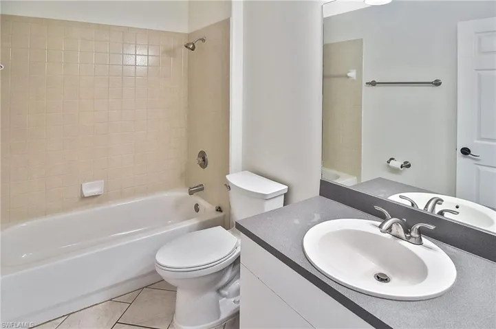 Full bathroom with tiled shower / bath combo, vanity, toilet, and tile patterned floors
