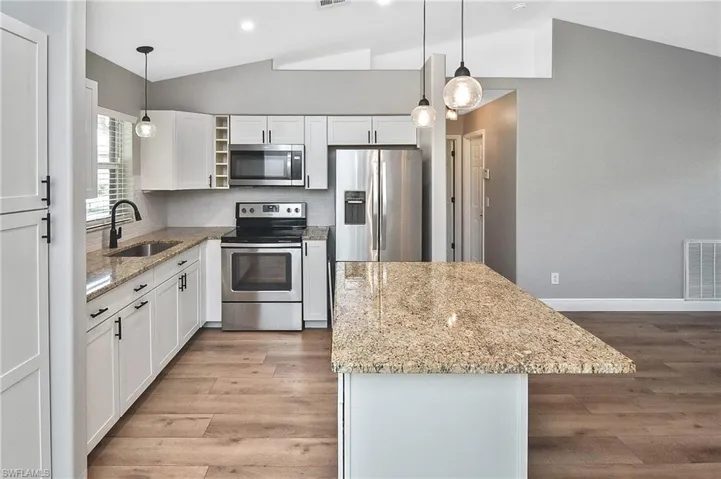 Kitchen featuring appliances with stainless steel finishes, hanging light fixtures, vaulted ceiling, white cabinets, and sink