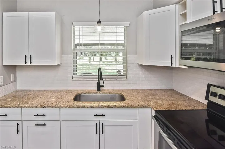 Kitchen with decorative backsplash, white cabinetry, stainless steel appliances, decorative light fixtures, and sink