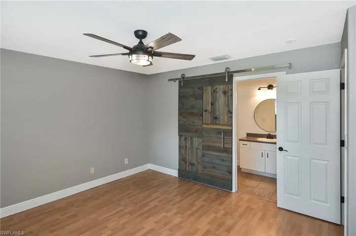 Unfurnished bedroom with a barn door, ceiling fan, light hardwood / wood-style flooring, and ensuite bathroom