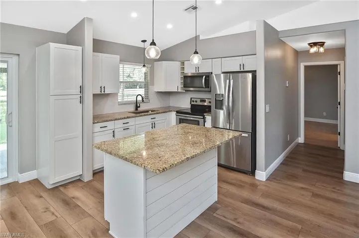 Kitchen with appliances with stainless steel finishes, white cabinets, light wood-type flooring, a center island, and sink