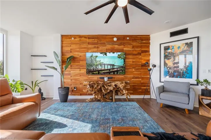 Living area featuring wood walls, an accent wall, wood finished floors, and ceiling fan