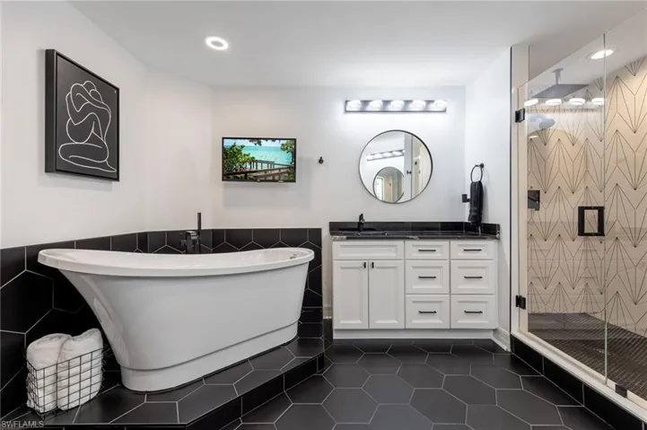 Full bath with tile walls, vanity, dark tile patterned flooring, a freestanding bath, and a stall shower