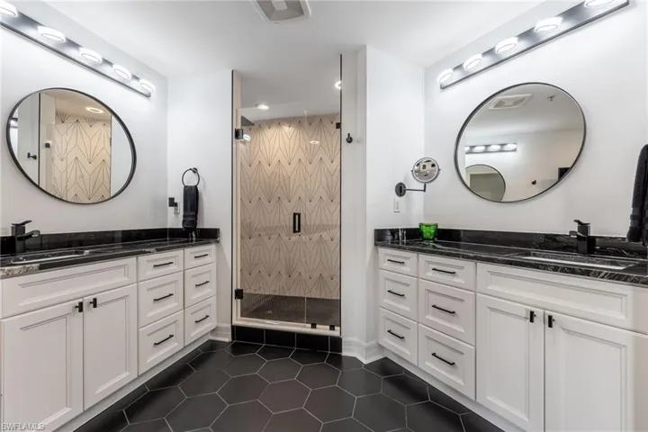 Bathroom with two vanities, dark tile patterned floors, a shower stall, and recessed lighting