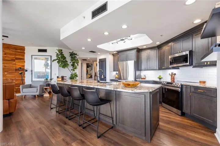Kitchen with a kitchen bar, light stone countertops, appliances with stainless steel finishes, a large island, and dark wood-style floors