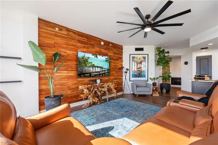 Living room featuring wooden walls, dark wood finished floors, ceiling fan, and an accent wall