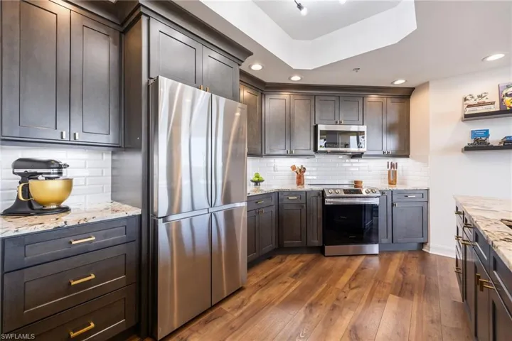 Kitchen with appliances with stainless steel finishes, light stone counters, dark wood-type flooring, tasteful backsplash, and recessed lighting