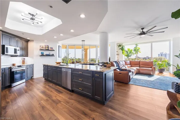 Kitchen featuring light stone countertops, backsplash, stainless steel appliances, open floor plan, and a tray ceiling
