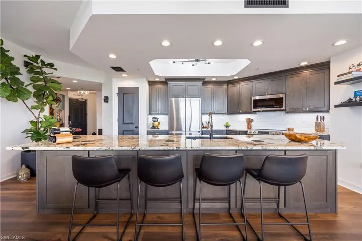 Kitchen with light stone counters, dark brown cabinetry, a breakfast bar area, decorative backsplash, and recessed lighting